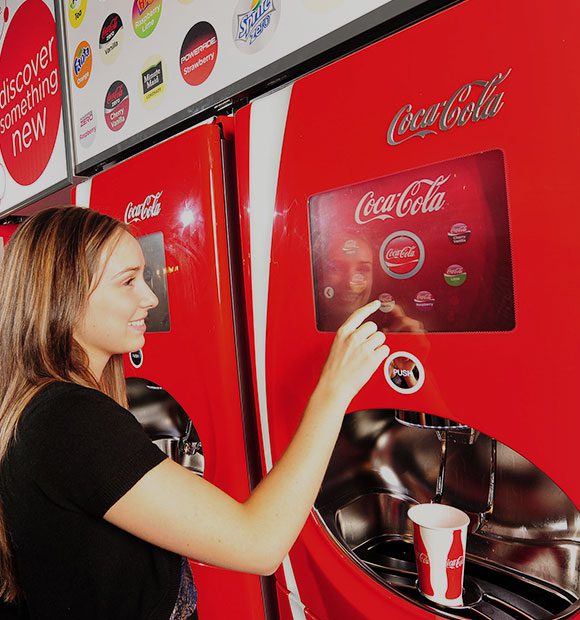 A woman is putting money into an automated coke machine.