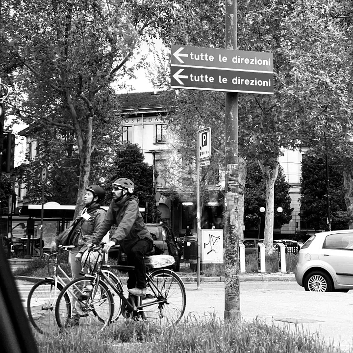 Two people riding bikes on a street near trees.